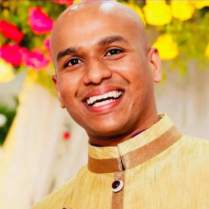 Portrait of author Tribue Francis, smiling, wearing a golden traditional jacket.
